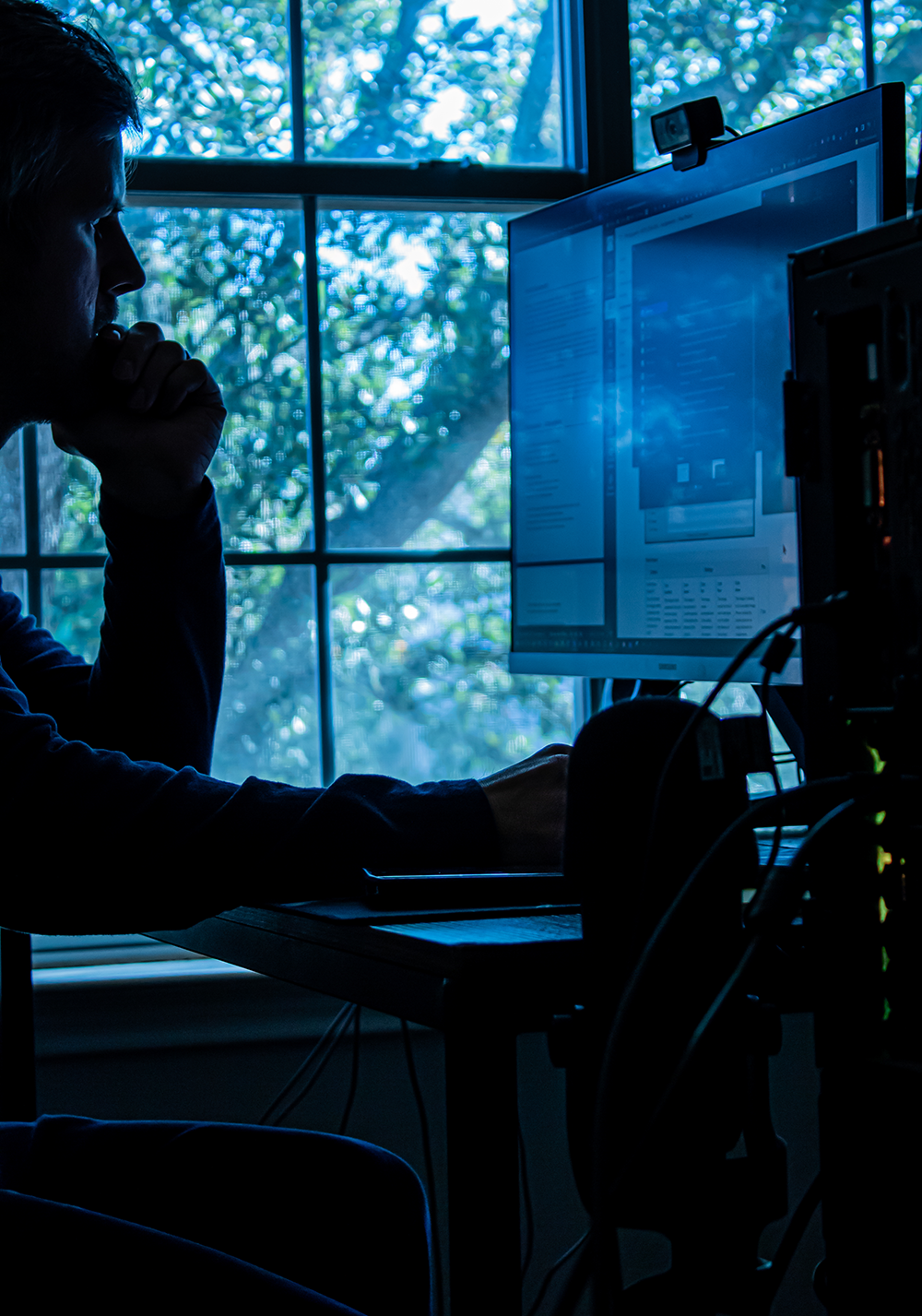 silhouette of a man at his computer desk in front of a window